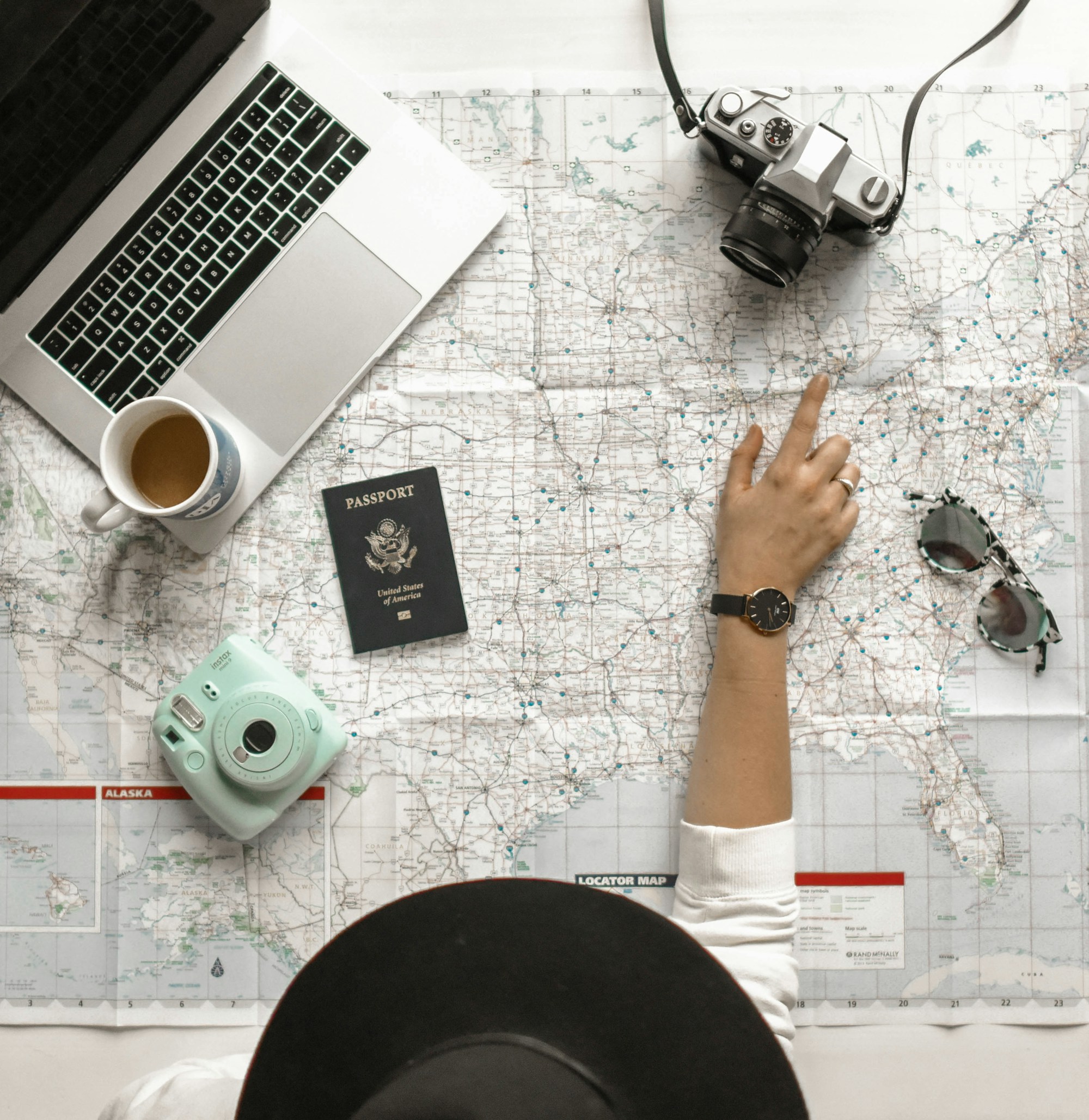A hand tracing a route on a road map spread across a desk beside a laptop